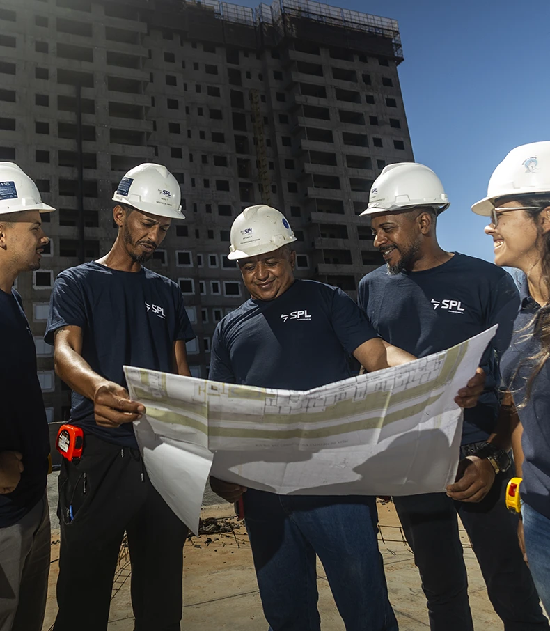 spl slide 1 Quatro jovens colegas de trabalho sorriem e colaboram em uma reunião em um escritório moderno, todos vestindo camisetas com o logo da SPL.